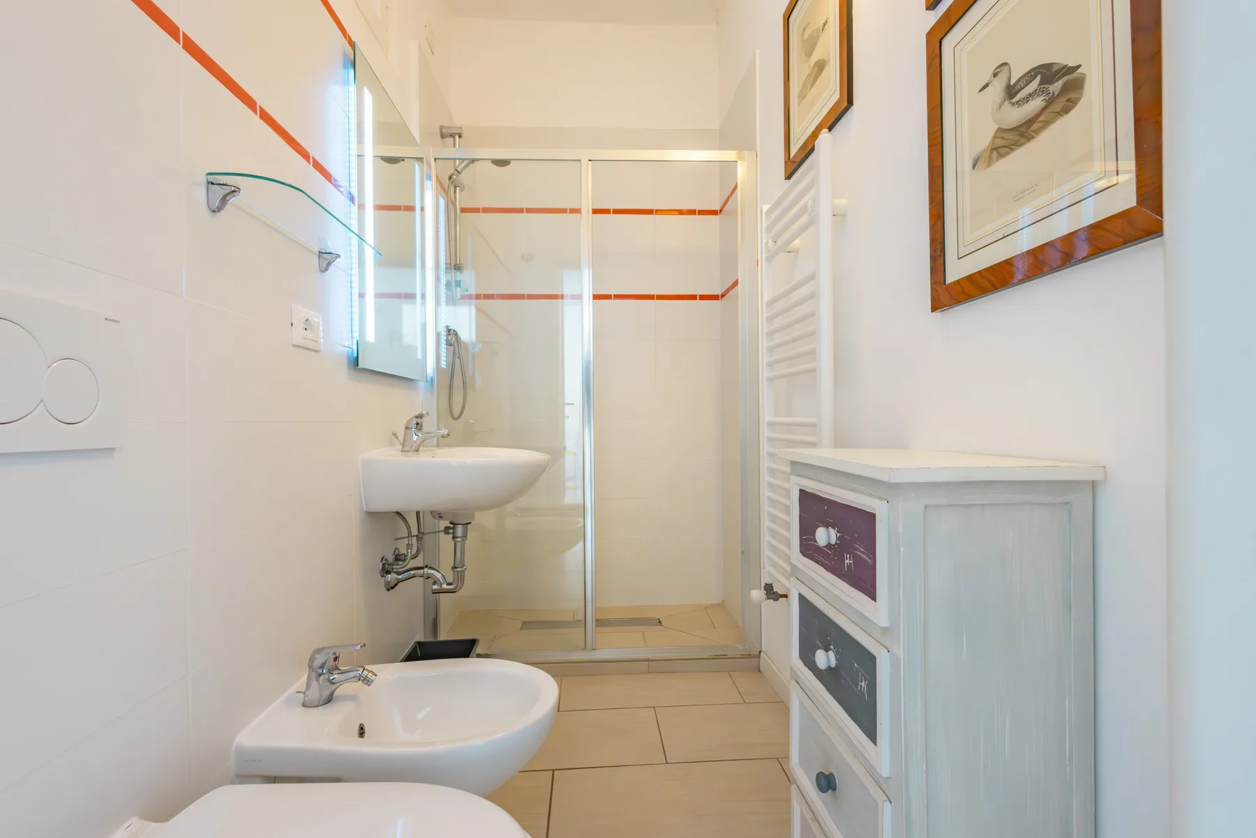 Un baño luminoso con ducha de vidrio, lavabo y cuadros enmarcados.