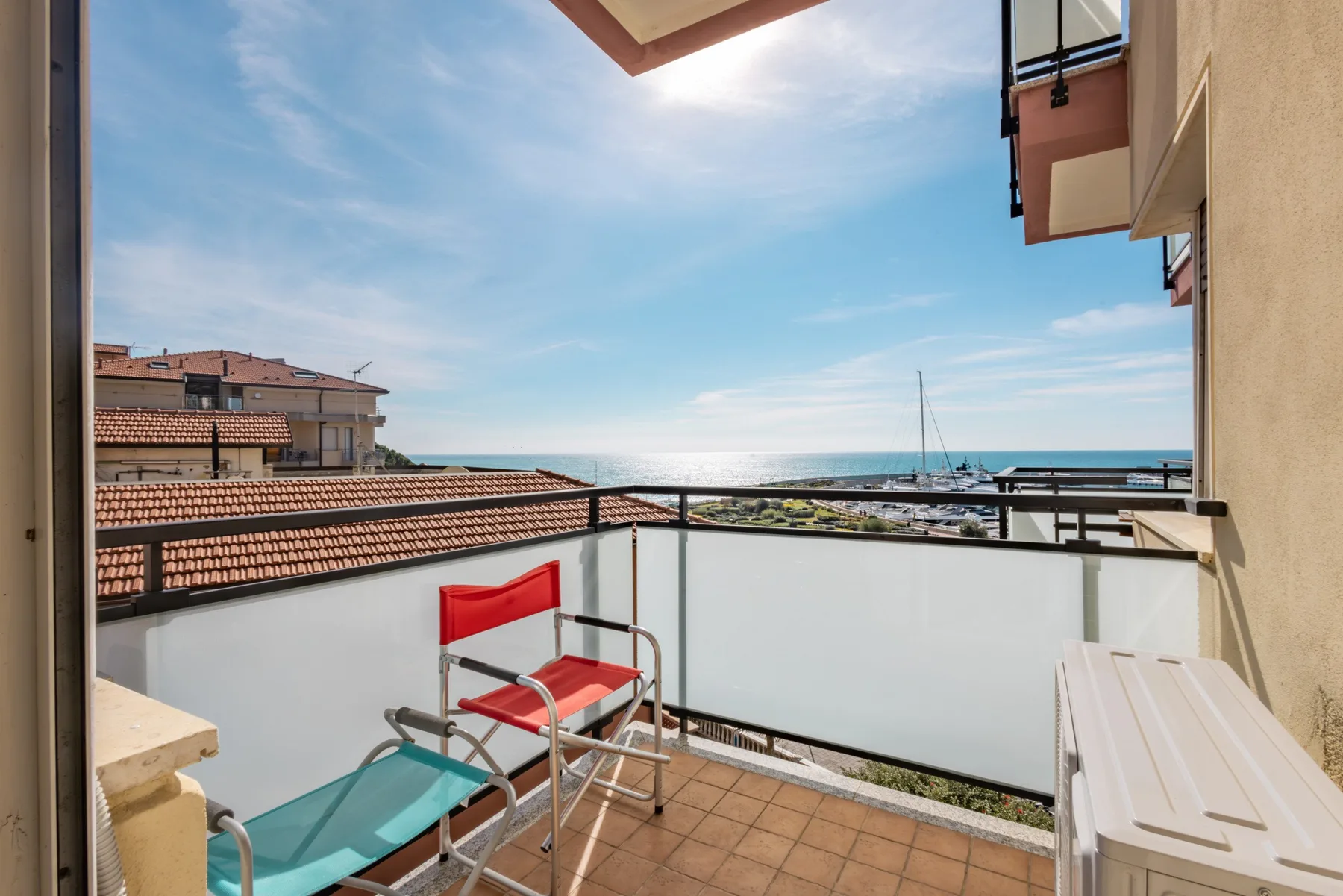 Un balcón soleado ofrece vistas de tejados cercanos y del mar.