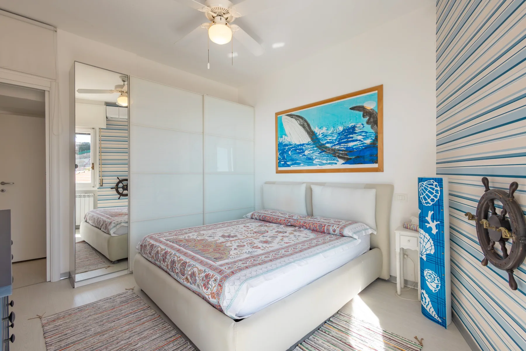 Un dormitorio luminoso con una cama arreglada y arte marino en la pared.