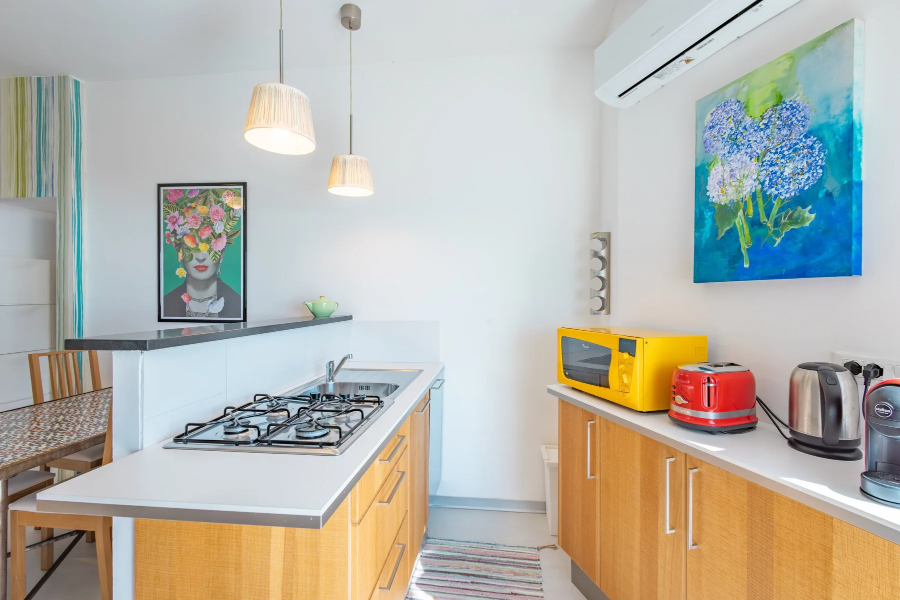Una cocina luminosa con una encimera central para cocinar y obras de arte coloridas en las paredes.