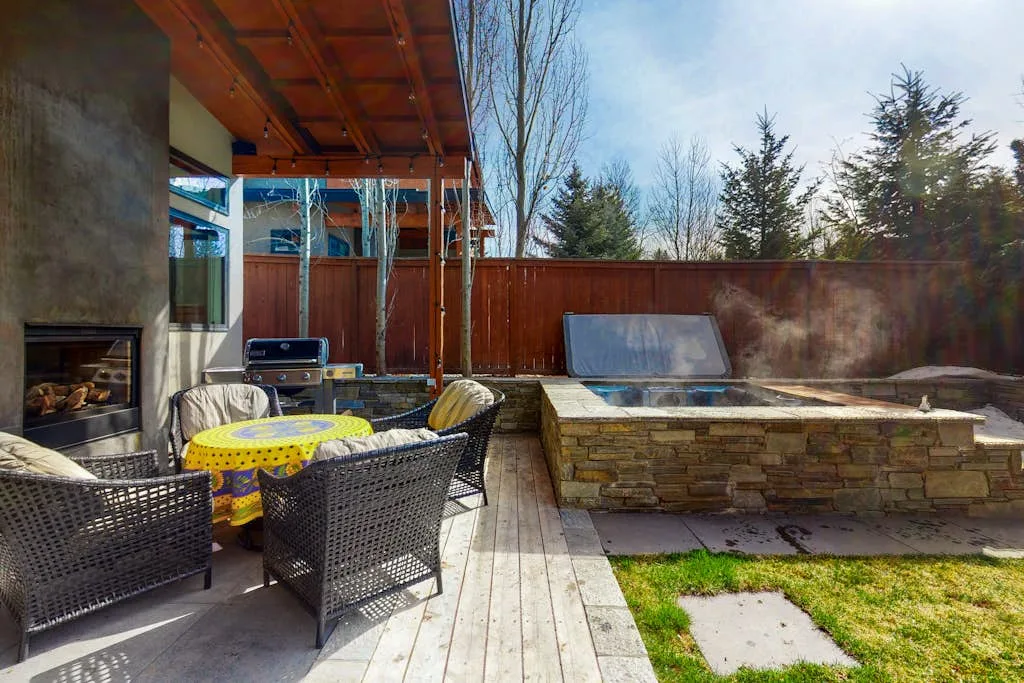 An outdoor patio with seating beside a raised stone spa and a wooden privacy fence.