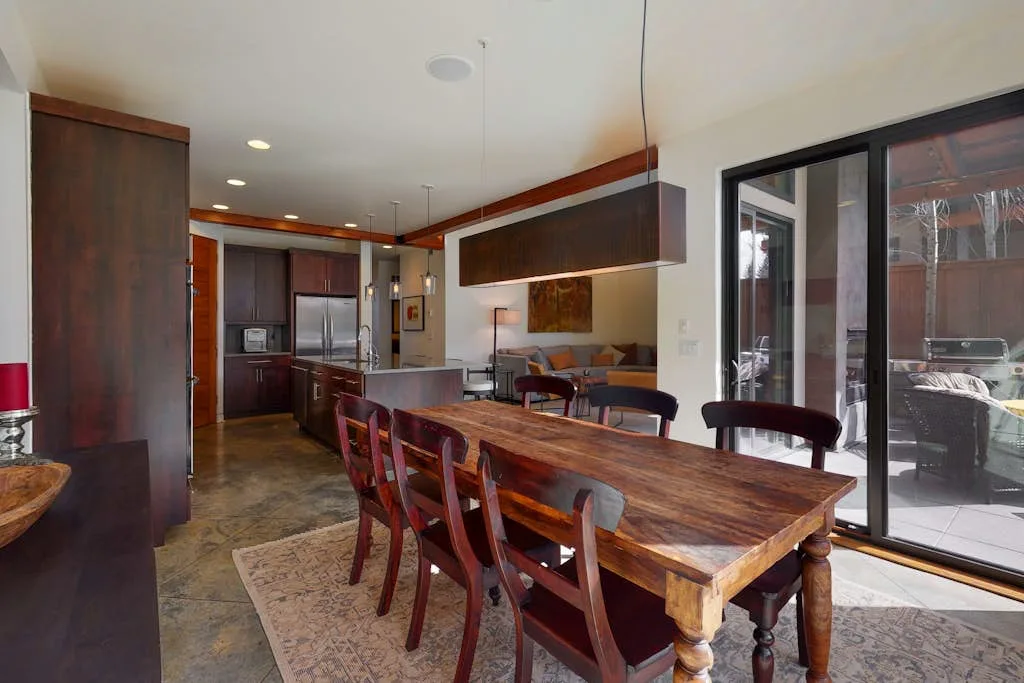 Comedor y cocina de concepto abierto, con una mesa larga de madera y puertas corredizas de vidrio.