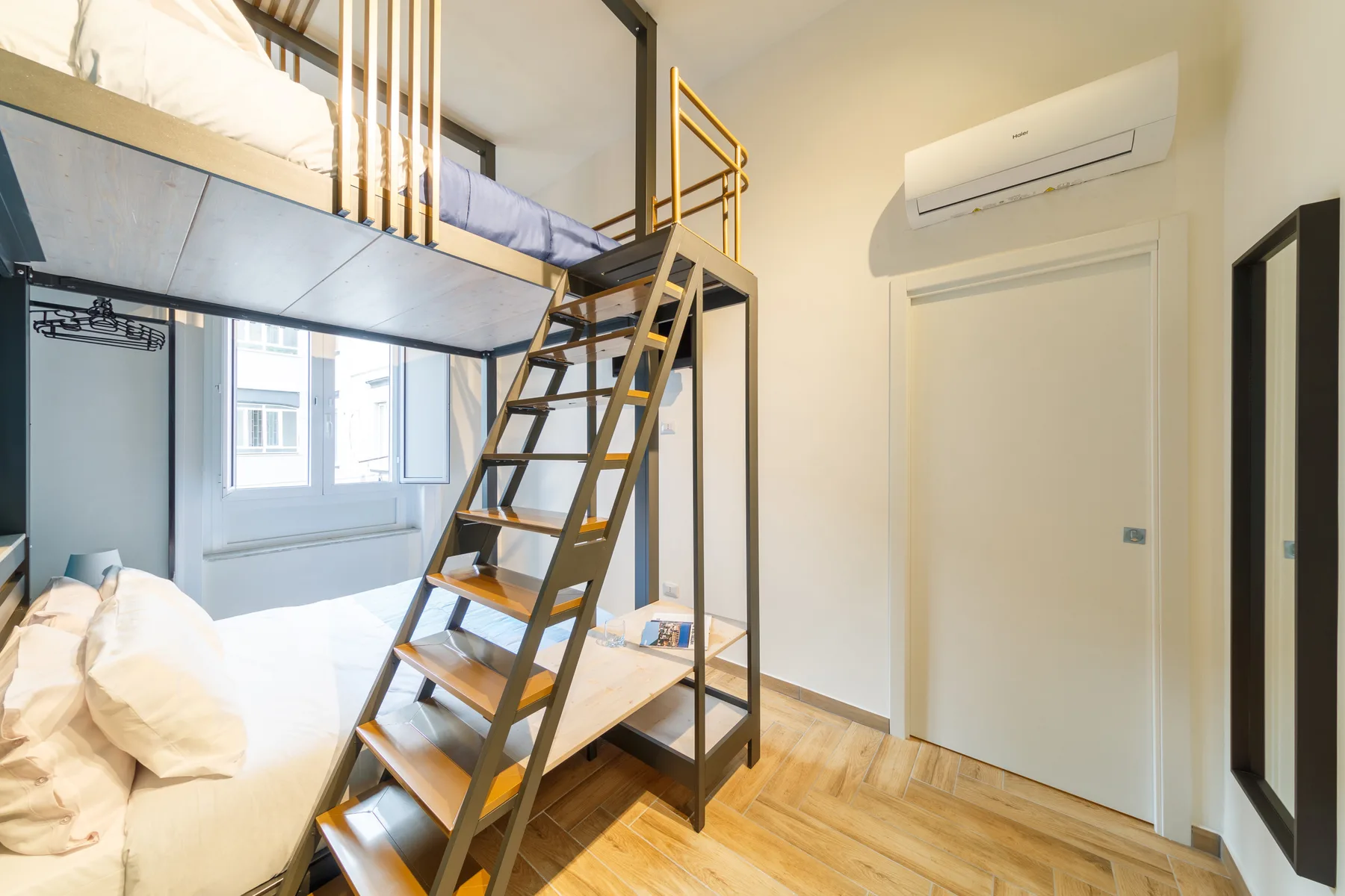 A bedroom with a raised sleeping area, ladder stairs, and a bed beneath the window.