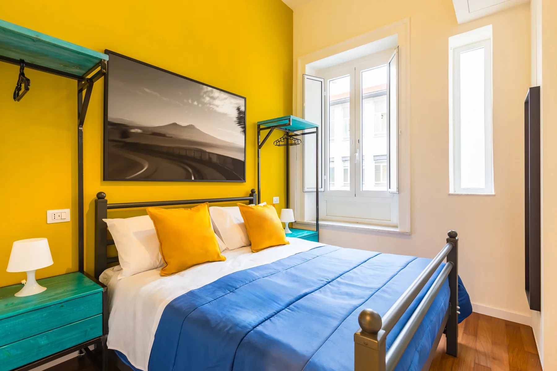 A bedroom with a bed dressed in blue and white bedding beneath a wall-mounted picture.