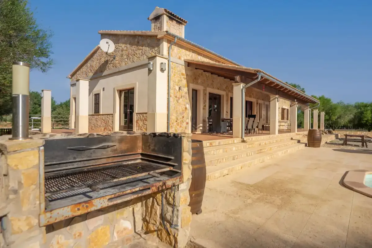 Casa de piedra con un porche cubierto y una barbacoa exterior integrada.