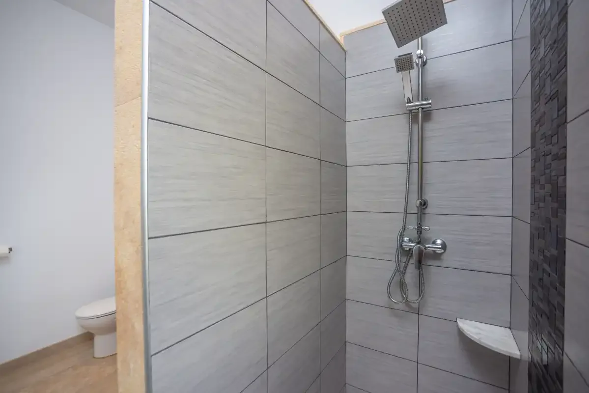 Una ducha de baño con azulejos, cabezal y controles montados en la pared.
