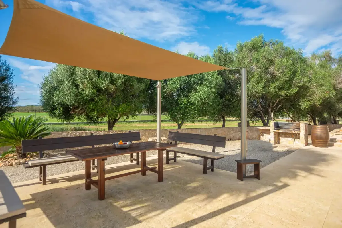 Una zona de comedor al aire libre está bajo una lona de sombra entre árboles.