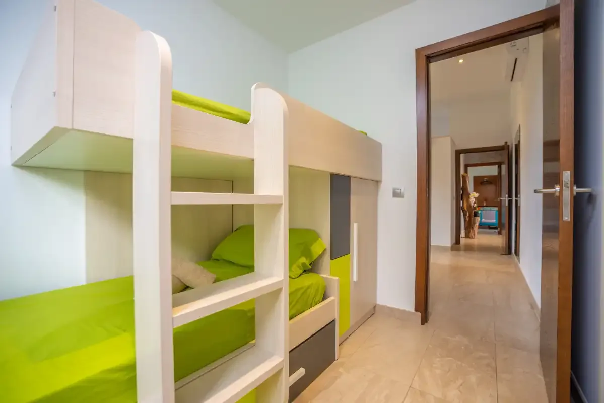 Un dormitorio con ropa de cama verde en literas junto a un pasillo.