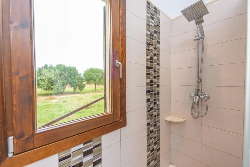 Un baño alicatado con ducha y una ventana con vistas a la vegetación.