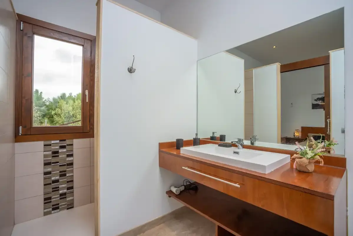 Un lavabo de baño con un espejo amplio y una ventana con vistas a la vegetación.