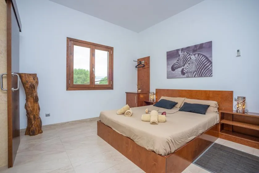 Un dormitorio con una cama hecha, un cuadro de cebras y una ventana con marco de madera.