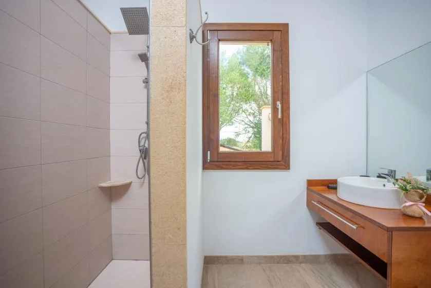 Un baño con ducha, una ventana y un mueble de lavabo de madera.