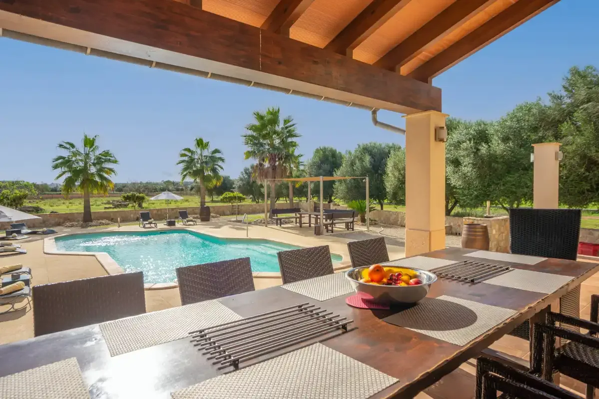 Una zona de comedor exterior cubierta da a una piscina y a un jardín.