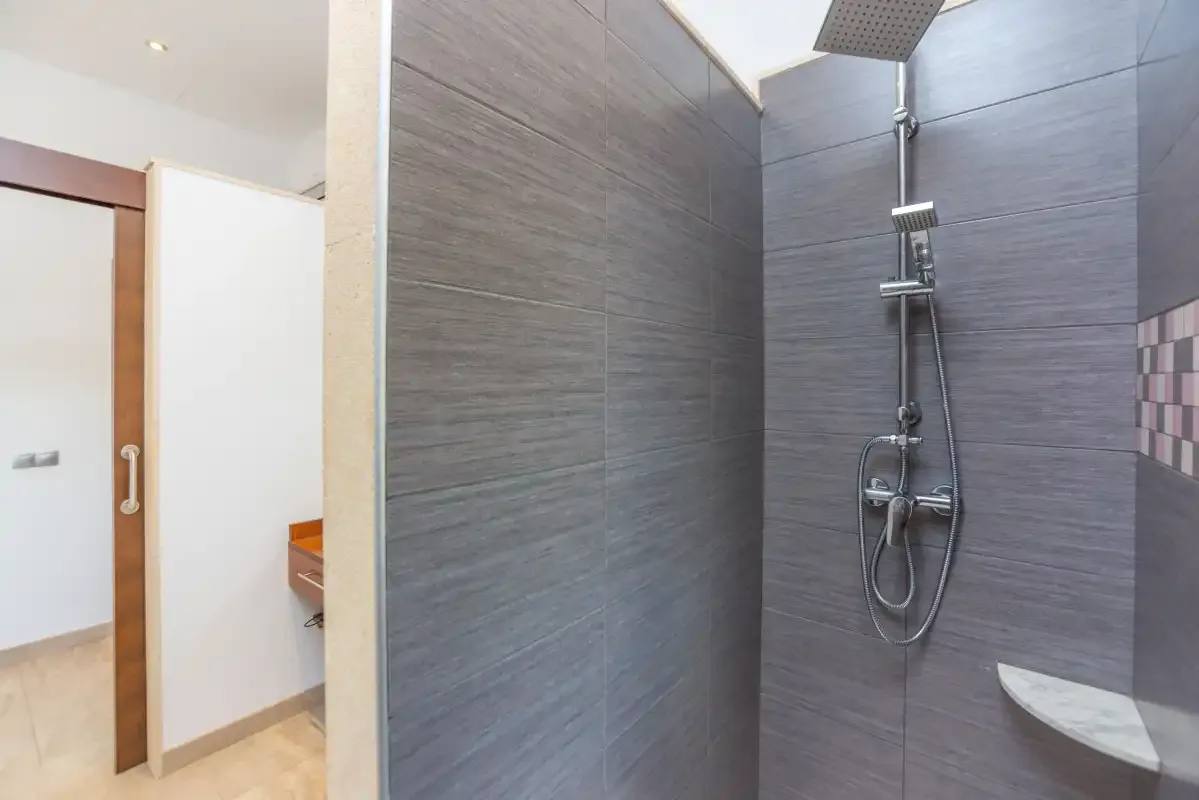 Un baño con ducha y azulejos grises en las paredes.