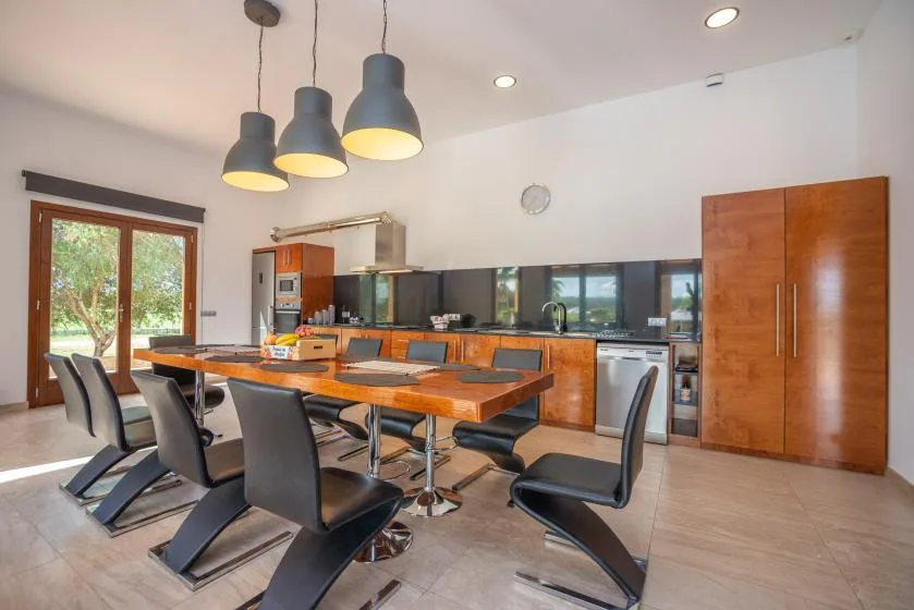 Un comedor con una mesa larga y sillas junto a una cocina.