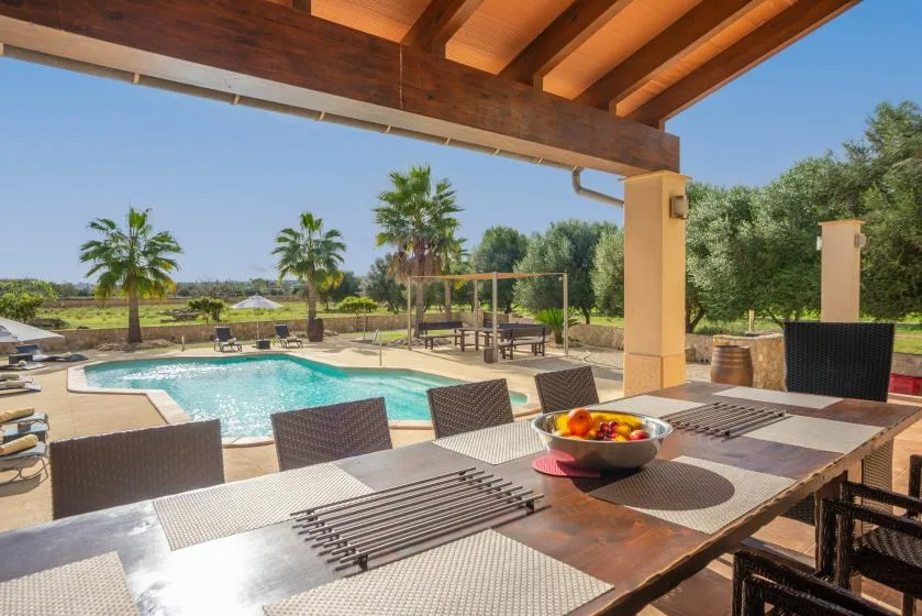 Una zona de comedor exterior cubierta da a una piscina y jardines.
