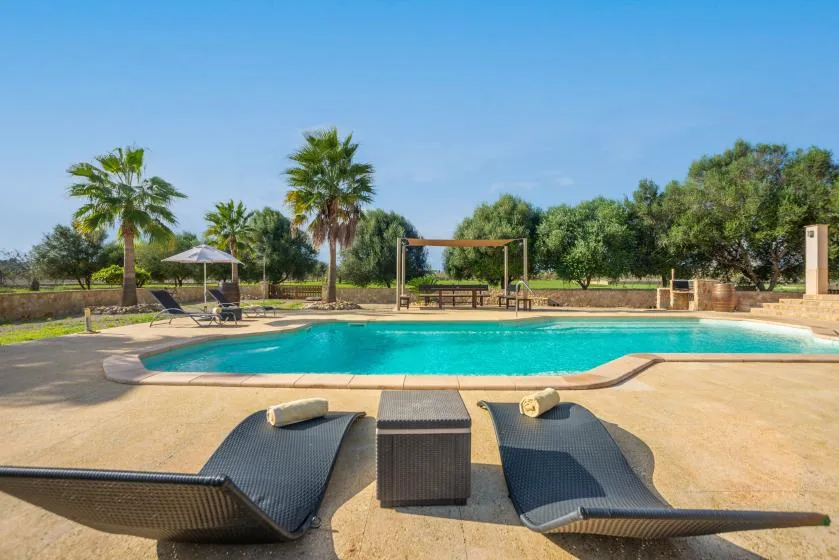 Una piscina al aire libre está rodeada por una terraza pavimentada y asientos reclinables.