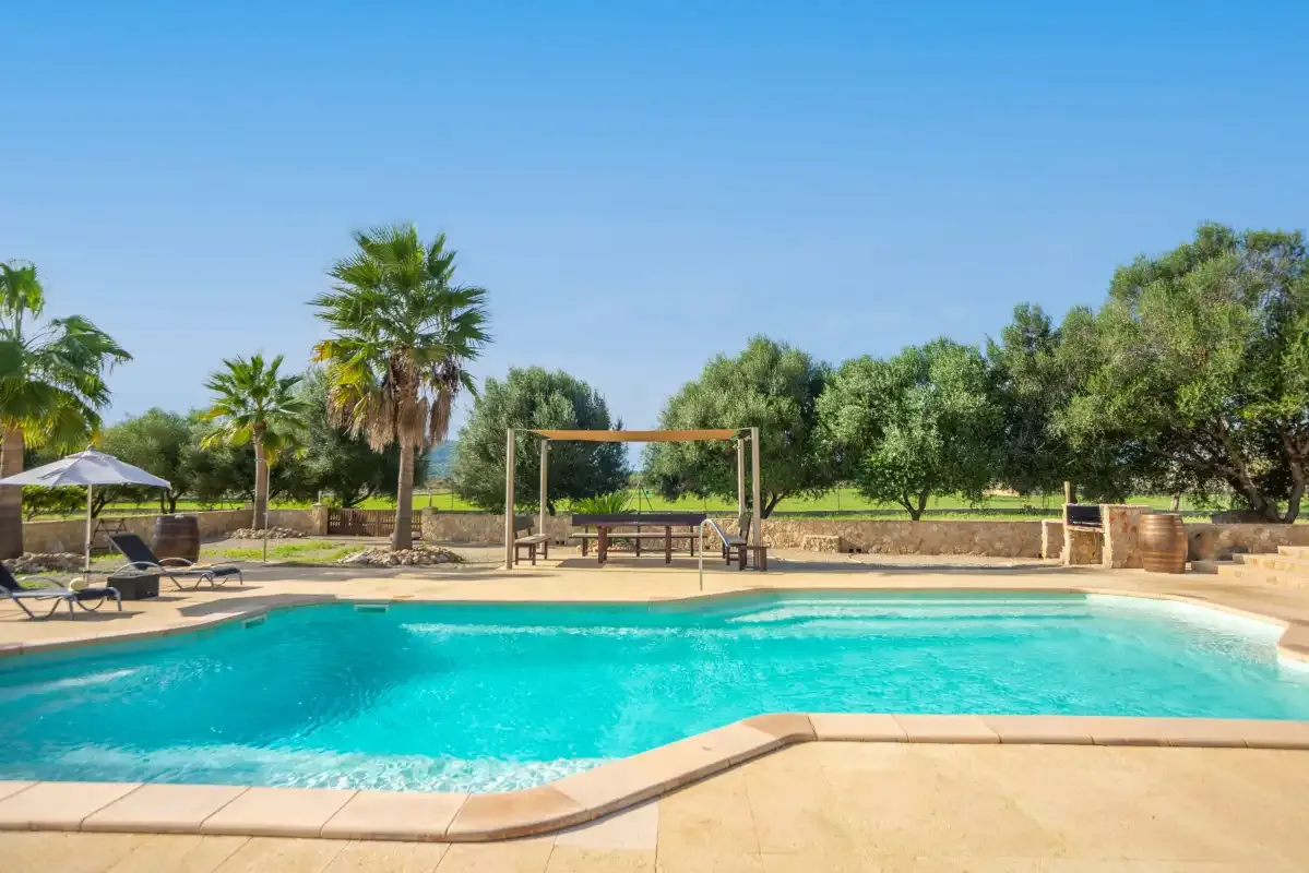 Una piscina al aire libre con una zona de estar sombreada y árboles cerca.