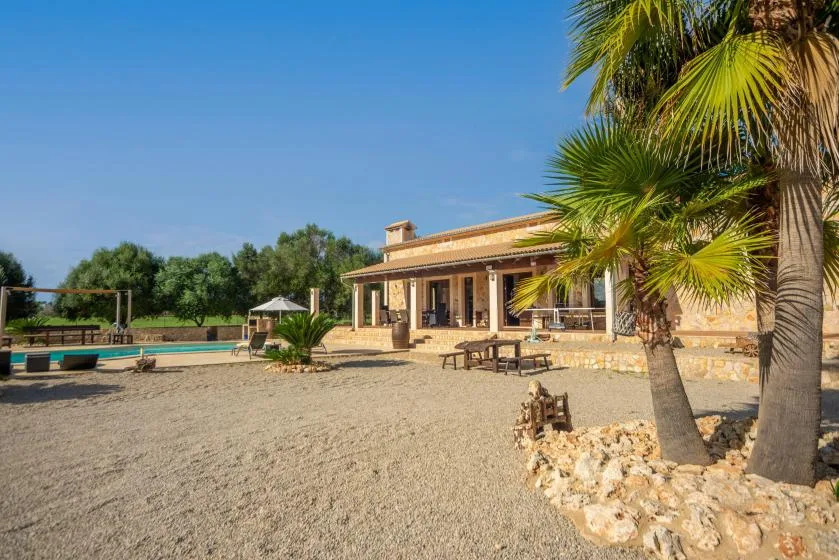 Una casa de piedra da a un patio de grava con palmeras y asientos al aire libre.