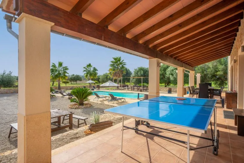Un patio cubierto con una mesa de ping-pong da a una piscina y un jardín.