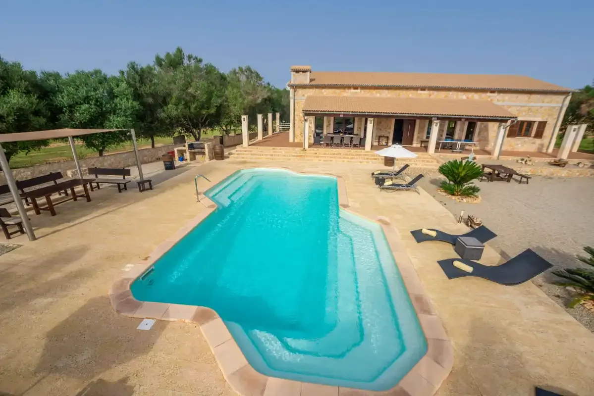Una piscina al aire libre está junto a un patio pavimentado y un edificio bajo.