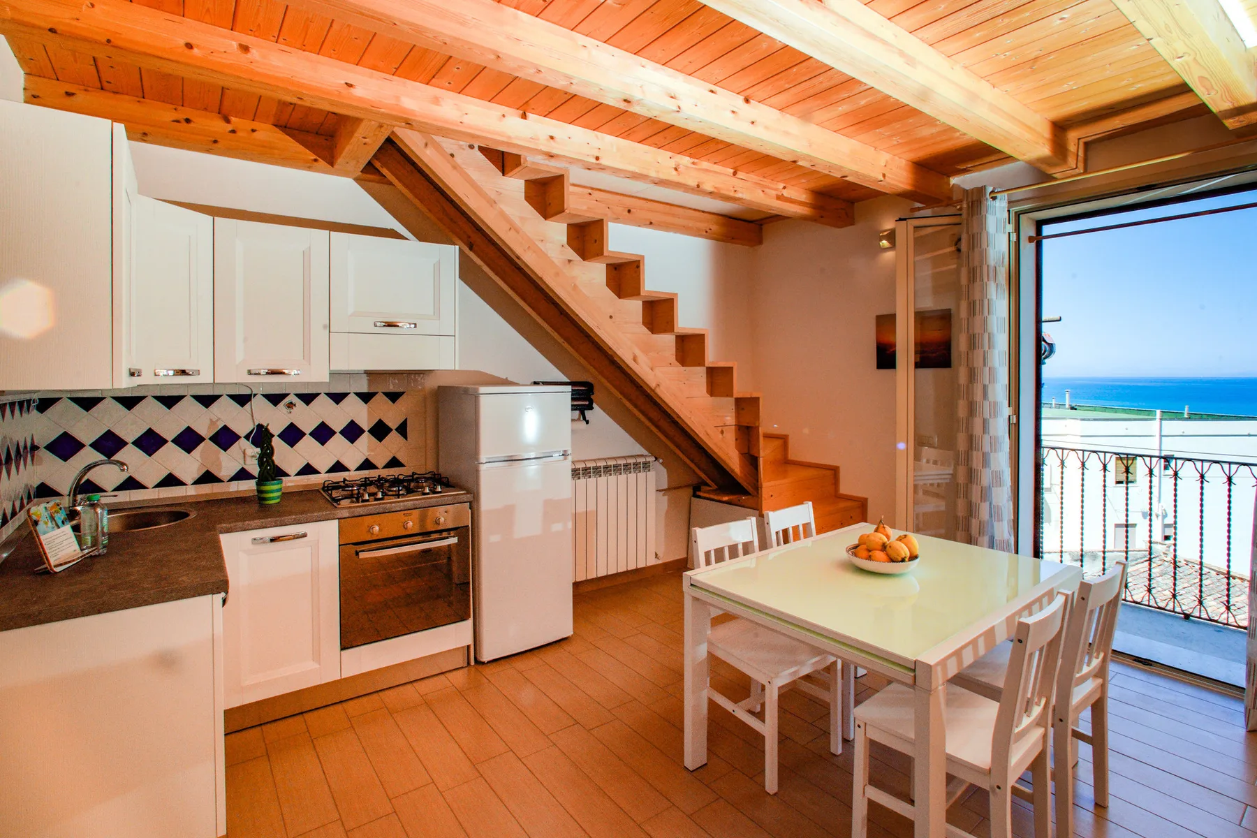 A kitchen and dining area with a table beside an open balcony doorway.