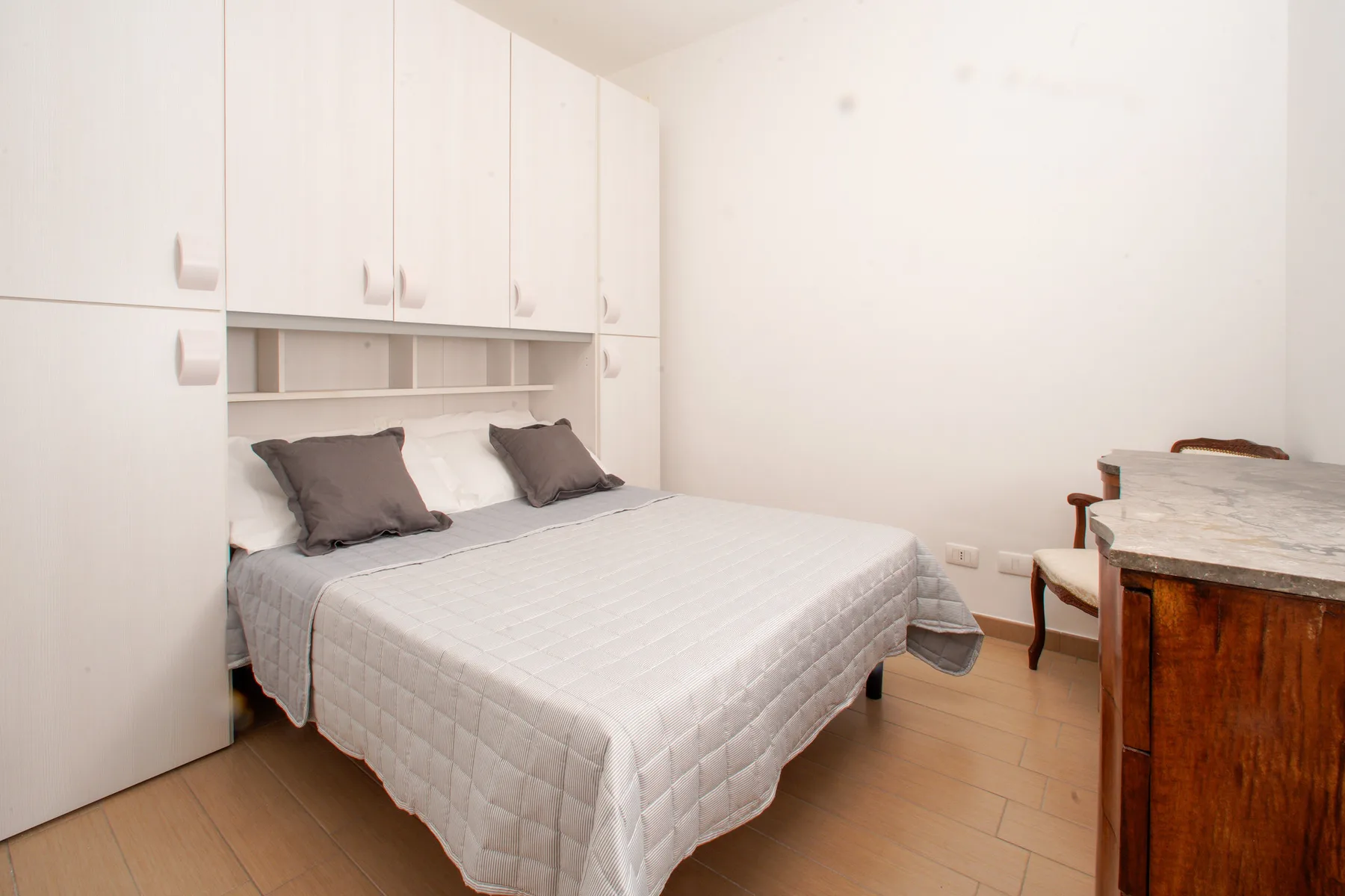 A bedroom with a double bed, white built-in cabinets, and a wooden table.