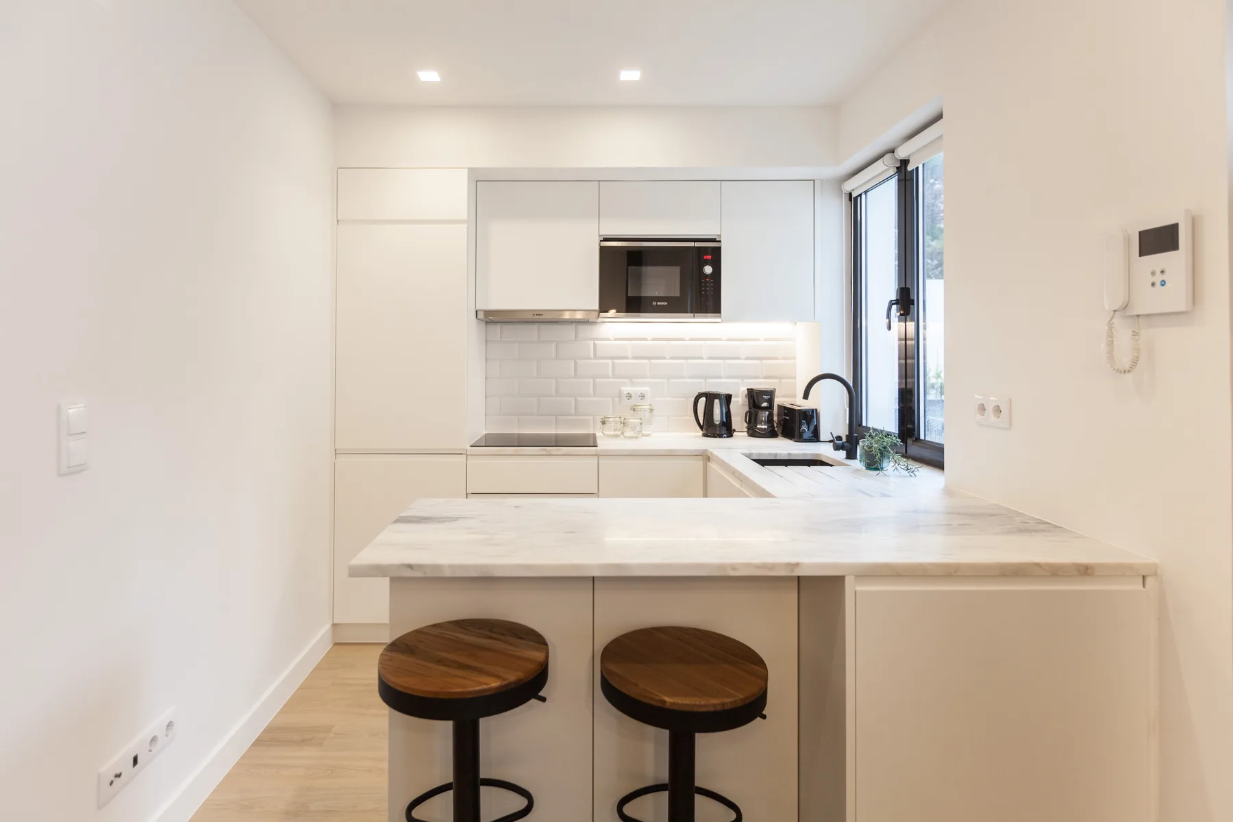 A bright studio kitchen with a breakfast counter and two stools.