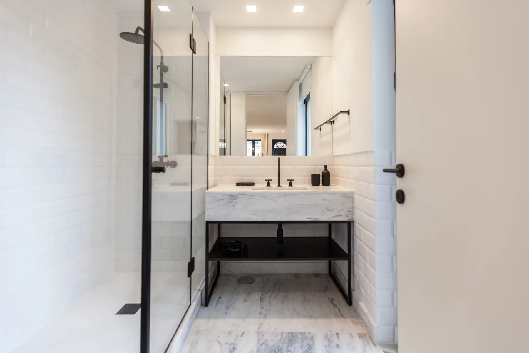 Un baño luminoso con una ducha de vidrio y un lavabo bajo un espejo grande.