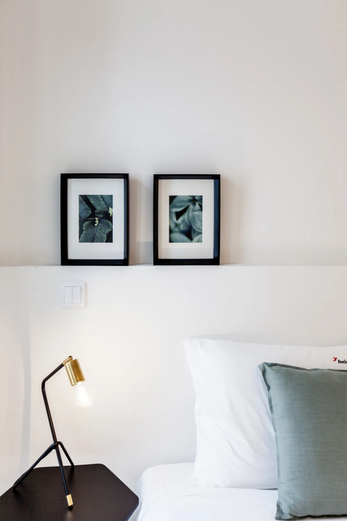 Un dormitorio con ropa de cama blanca, un cojín azul y cuadros enmarcados sobre la cama.