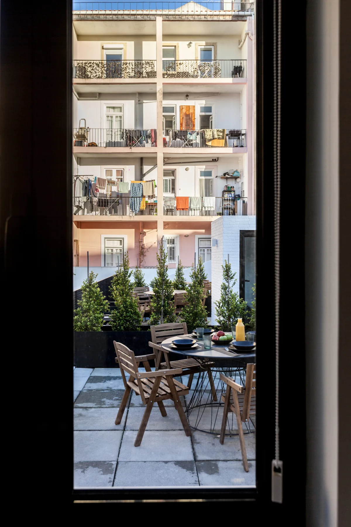 Una zona de comedor en el patio da a un edificio de apartamentos con balcones.