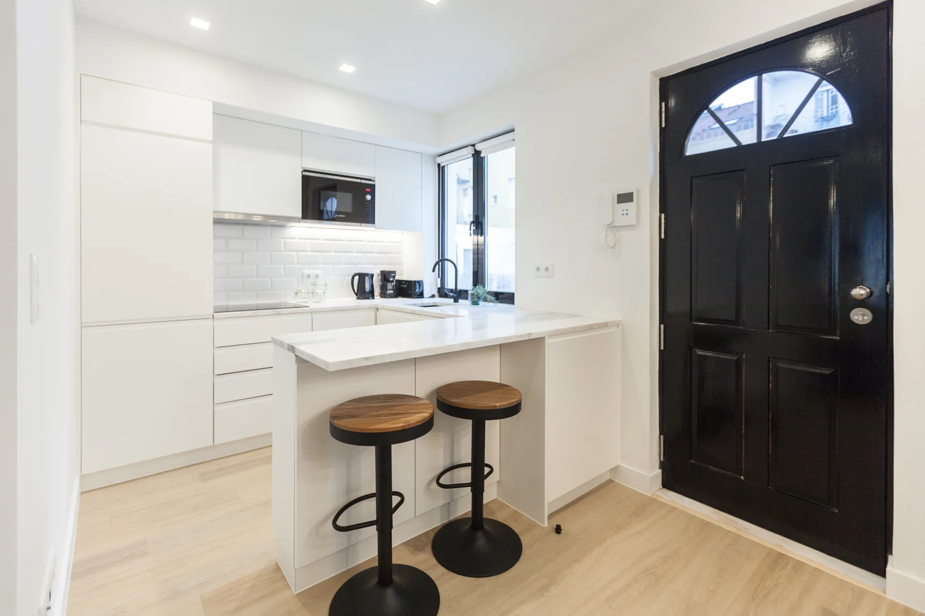 Cocina luminosa con una isla blanca y dos taburetes junto a una puerta negra.