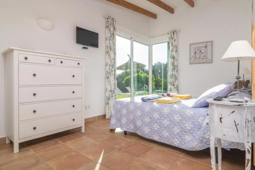 Un dormitorio luminoso con una cama junto a grandes ventanas con vistas a la vegetación.