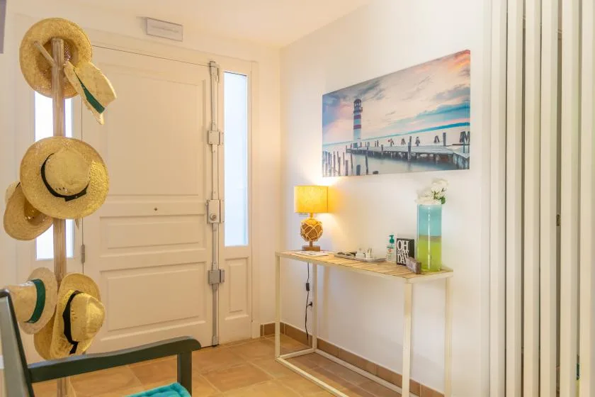 Una entrada luminosa con una consola estrecha, una lámpara y arte costero en la pared.