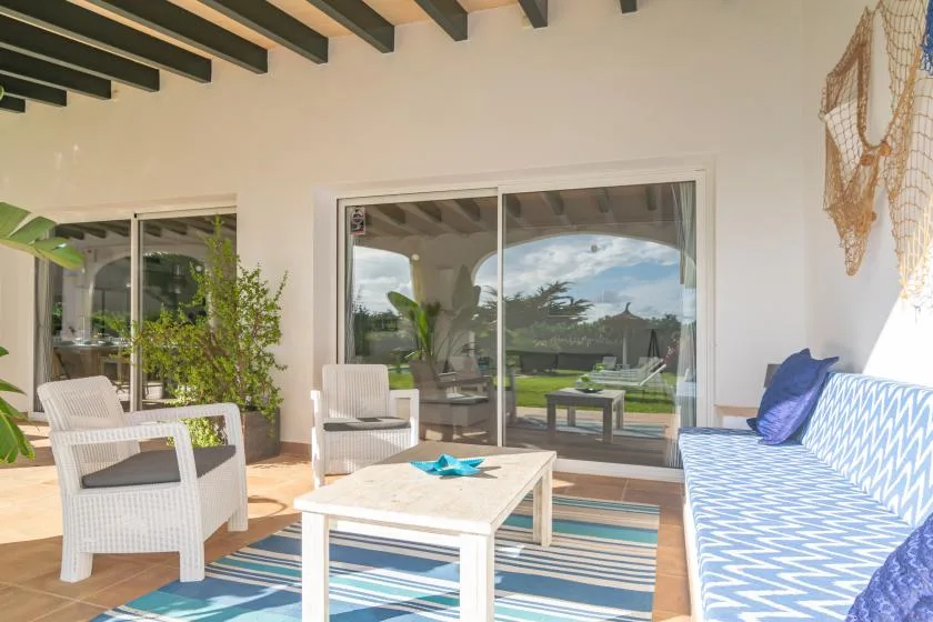 Un patio cubierto tiene asientos alrededor de una mesa baja junto a puertas corredizas de vidrio.