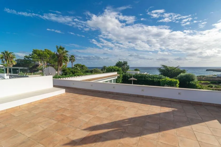 Una terraza de baldosas da a palmeras y al mar bajo un cielo parcialmente nublado.