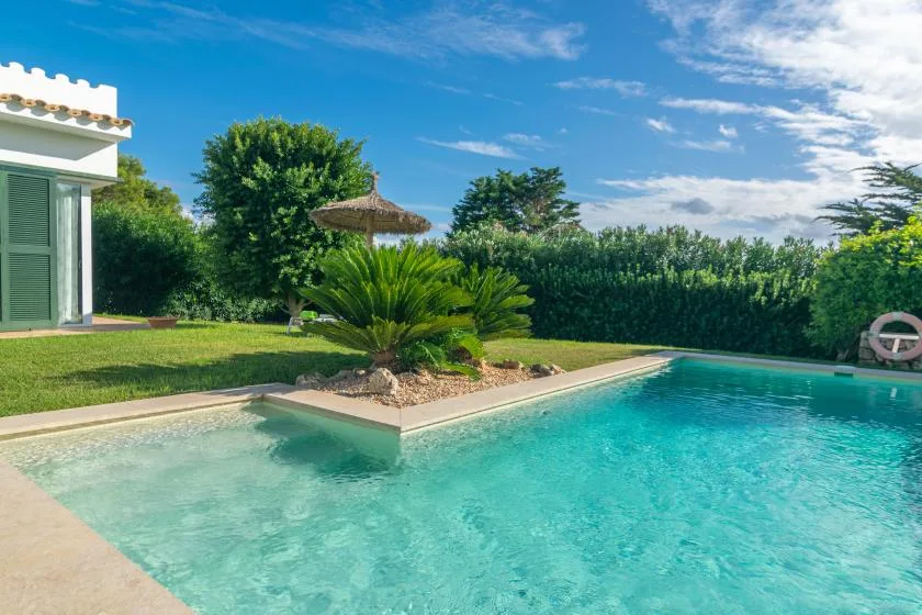 Una piscina al aire libre junto a un césped y un jardín ajardinado.
