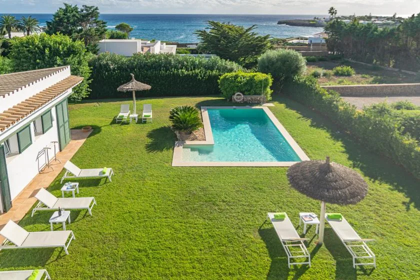 Un jardín con piscina y el océano visible al fondo.
