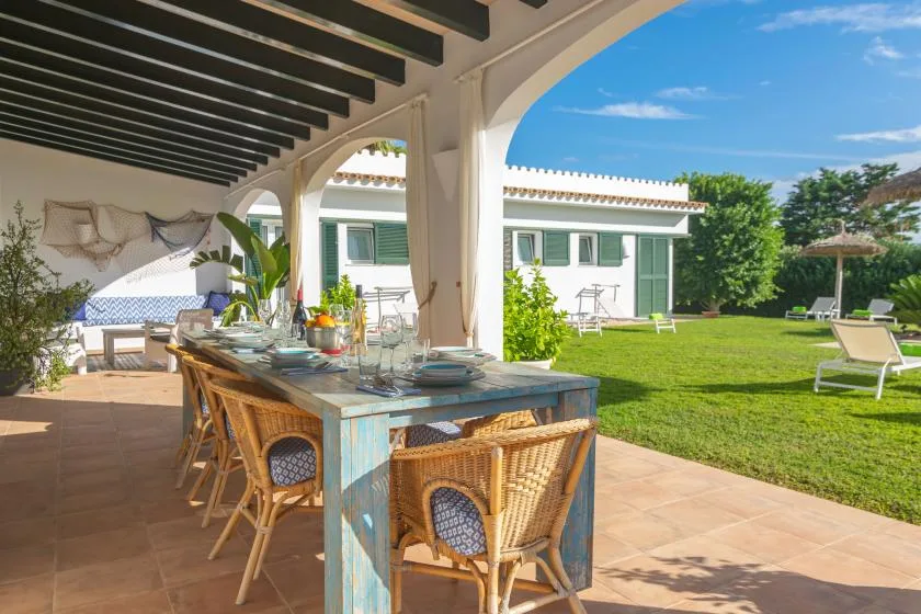Una zona de comedor exterior cubierta da a un césped verde con asientos.