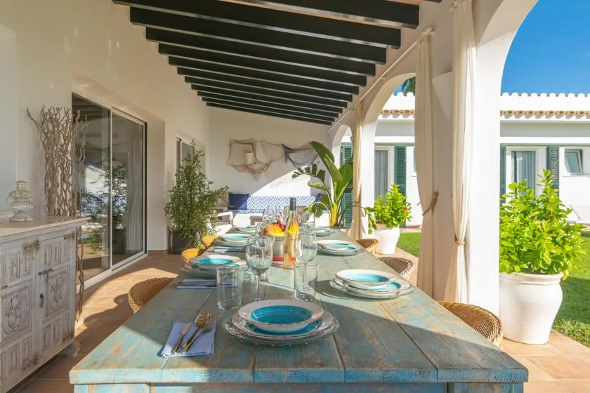 Comedor exterior cubierto con una mesa larga preparada para comer.
