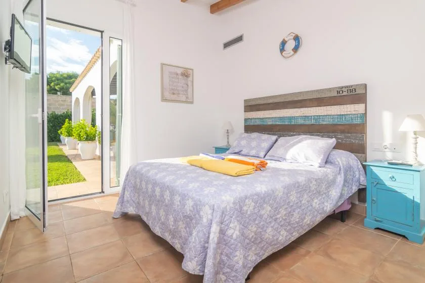Un dormitorio con una cama grande junto a puertas de vidrio abiertas que dan al jardín.
