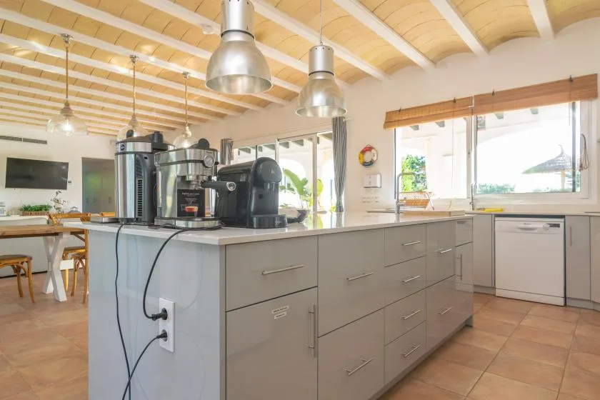 Una cocina luminosa con una isla central, equipo de café y grandes ventanas.