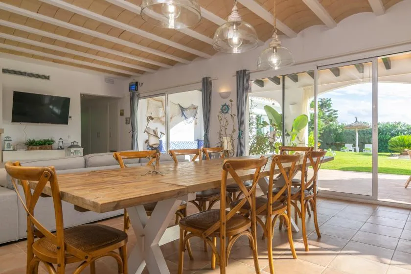 Comedor con una larga mesa de madera y puertas corredizas de vidrio que dan a un jardín.