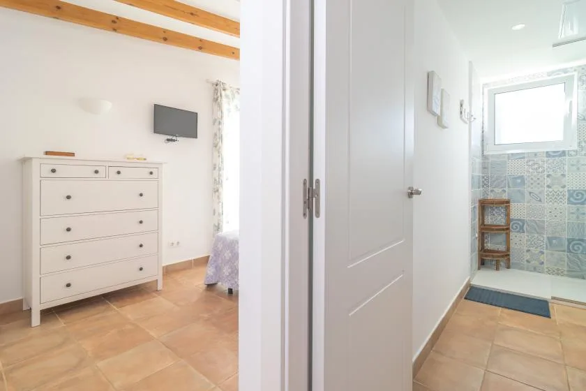 Un dormitorio con una cómoda blanca da a un baño con azulejos y una ventana.