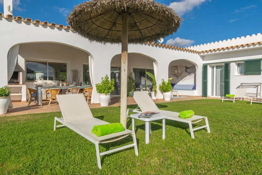 Un patio soleado con asientos, una sombrilla de paja y aberturas arqueadas.
