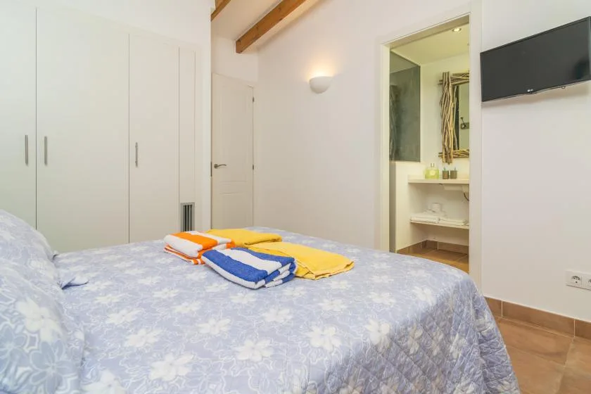 Un dormitorio con una colcha floral y toallas dobladas junto a un baño abierto.