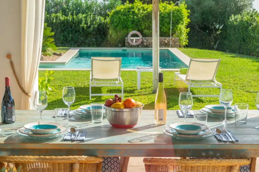 Una mesa está puesta junto a una piscina en el jardín, con sillas sobre el césped.