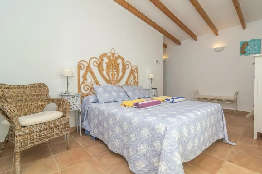 Un dormitorio con una cama doble, asiento de mimbre y vigas de madera a la vista.