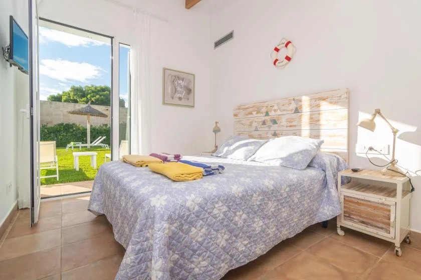Un dormitorio luminoso con una cama grande y una puerta de vidrio abierta al jardín.