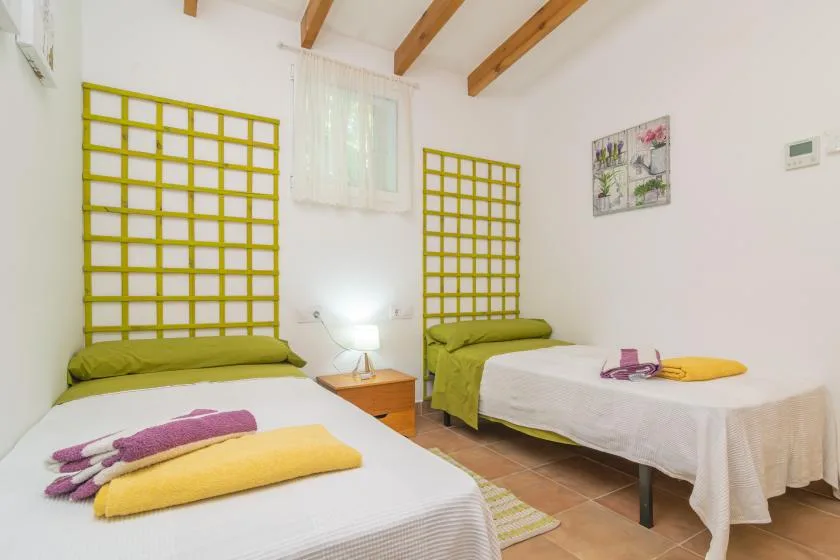 Un dormitorio luminoso con dos camas, cabeceros amarillos de celosía y vigas de madera a la vista.